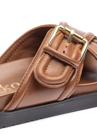 Sandal in pelle marrone con fascia ampia e fibbia decorativa. Include una soletta testurizzata e una suola in gomma nera.