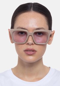 Occhiali da sole oversize beige con montatura quadrata e lenti leggermente oscurate, caratterizzati da aste spesse e una texture opaca.