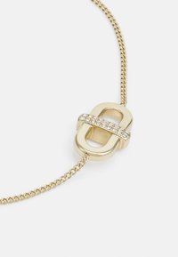 Goldene Halskette mit einem ovalen Anhänger, der ein horizontales Band aus klaren Kristallen aufweist, befestigt an einer gedrehten Kette.