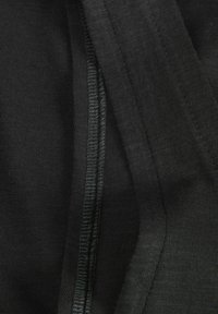 Tejido negro, ligero y con una textura suave. Presenta una costura visible y acentos acanalados, adecuado para superponer o para uso casual.