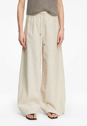 Weite beige Leinenhose mit Kordelzugbund, getragen mit braunem Stricktop und schwarzen Sandalen mit quadratischer Spitze.