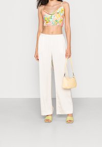 Crop top floreale in tonalità pastello; pantaloni larghi crema; borsa gialla chiara; sandali con tacco blocco verdi; texture del tessuto liscia.