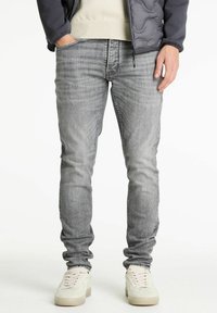 Jeans de mezclilla gris ajustados con una textura deslavada, diseño de cinco bolsillos y detalles de costura mínimas, combinados con zapatillas blancas.