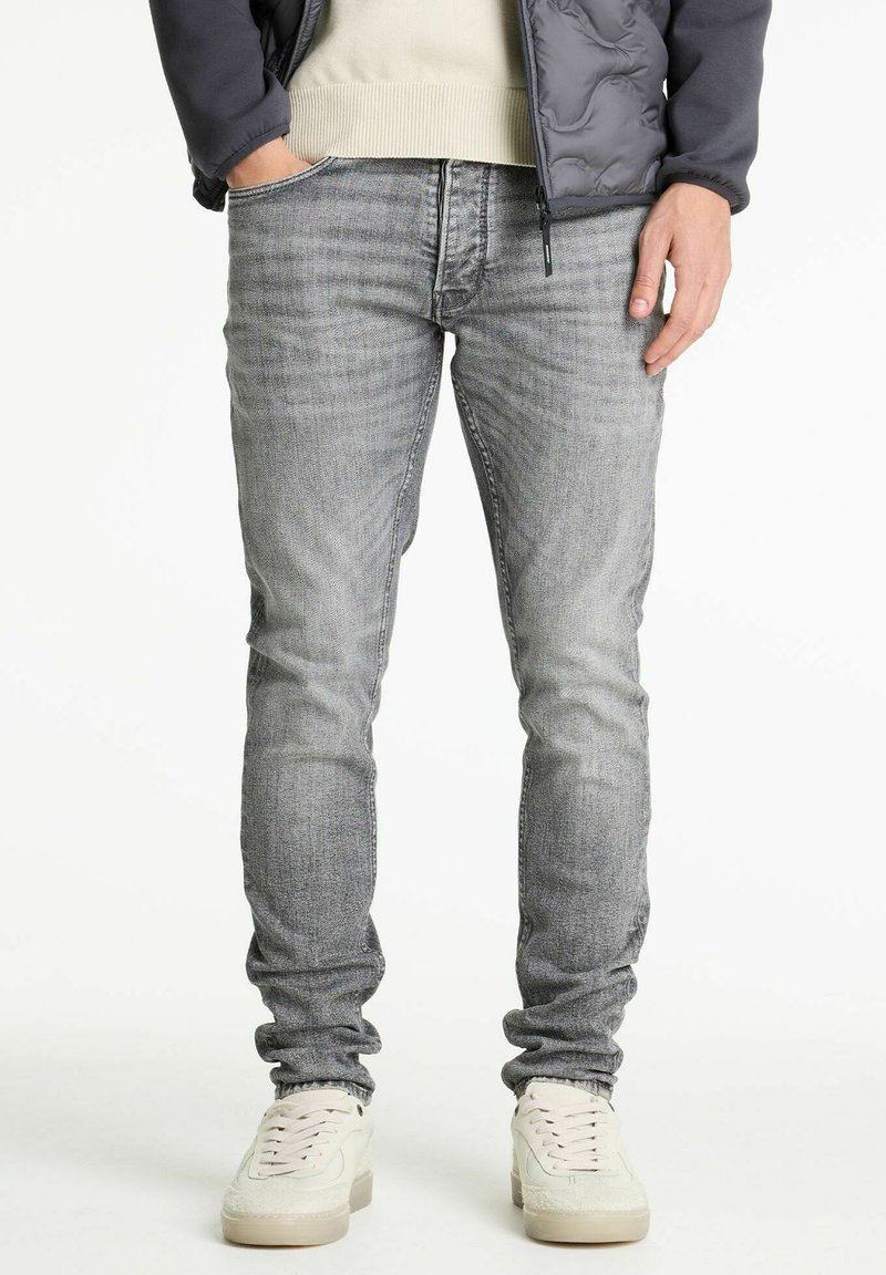 Jeans de mezclilla gris ajustados con una textura deslavada, diseño de cinco bolsillos y detalles de costura mínimas, combinados con zapatillas blancas.