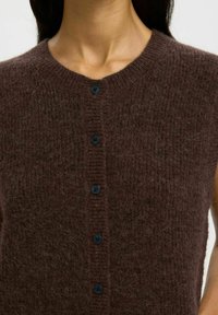 Brązowy, dzianinowy, bezrękawnik z okrągłym dekoltem i pięcioma ciemnymi guzikami z przodu; miękka tekstura z lekko puszystą powierzchnią.
