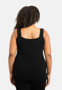 Svart ärmlös topp med breda remmar, fyrkantig halsringning och ribbad nederdel. Tillverkad av ett mjukt, stretchbart material med en figurnära siluett.