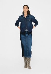 Tamsiai mėlyna džinsinio audinio marškiniai ilgomis rankovėmis ir dviem krūtinės kišenėmis. Ilgas džinsinis sijonas su nėrinių įsiuvais šonuose. Batai su gyvatės odos raštu.