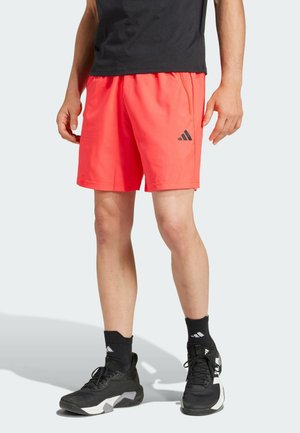 Pantaloni sportivi da uomo in corallo con vita elastica, tasche laterali e logo Adidas nero. Indossati con scarpe da ginnastica nere e calze.