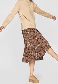 Felpa beige con cappuccio e lacci abbinata a una gonna leopardata marrone. La gonna presenta un orlo svasato e un tessuto leggero. Scarpe platform color marrone chiaro.