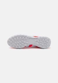 Semelle de chaussure de soccer rouge et blanche avec des picots en caoutchouc texturé pour une meilleure adhérence, arborant le logo "PREDATOR" et un design de blocs de couleur distinct.