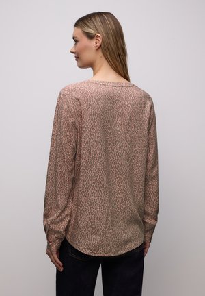 Blouse à manches longues en marron clair avec un motif léopard subtil. Tissu doux, ourlet arrondi et manches légèrement bouffantes.