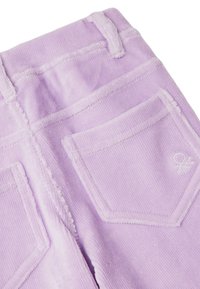 Lila spodnie z korduroju z widocznymi szwami, dwiema tylnymi kieszeniami i małym haftowanym logo na górnej prawej kieszeni.