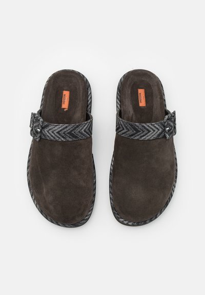 Barna velúr slip-on klumpák, fekete chevron mintás pánttal, dekoratív csattal és texturált talpbéléssel.