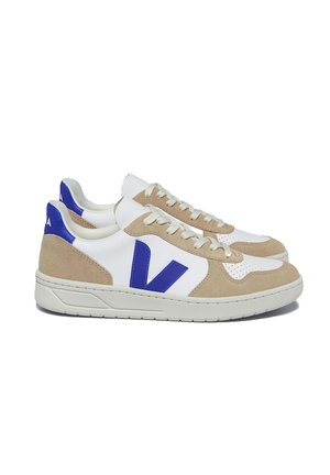 Sneakers featuring a white leather upper, beige suede accents, and blue logo. Lace-up design with perforated detail on the toe. Rubber sole.