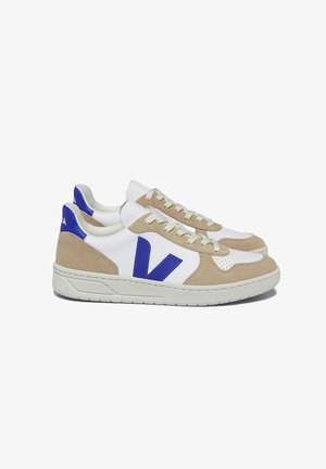 Sneakers featuring a white leather upper, beige suede accents, and blue logo. Lace-up design with perforated detail on the toe. Rubber sole.