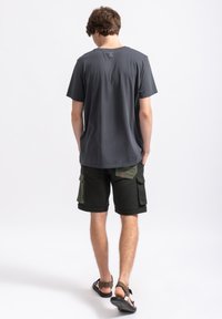 Grijze katoenen T-shirt, korte mouwen, ronde hals, met een klein logo-detail op de achterkant. Gecombineerd met donkergroene cargoshorts.