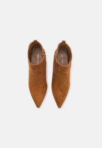 Botas de tobillo de ante marrón con puntera afilada, cremalleras laterales y una lengüeta para facilitar el calzado, con una textura suave.