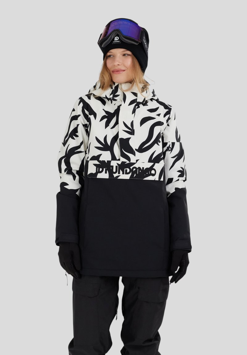 Donna che indossa una giacca da sci a righe bianche e nere, pantaloni da neve neri, guanti neri, un berretto nero e occhiali da sci viola sulla testa.