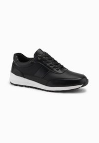 Scarpe da ginnastica nere con una parte superiore testurizzata, che presenta una punta in pelle liscia, una suola intermedia bianca e una suola in gomma nera. I lacci sono neri.