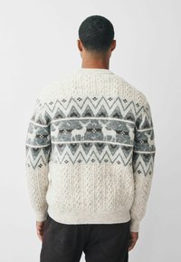 Strickpullover in Creme mit strukturiertem Muster, das ein geometrisches Design in Grau mit Rentiermotiven zeigt. Rippbündchen und Saum.