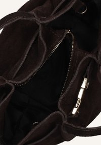 Bruine suède handtas met een ruime, zwarte stoffen binnenkant. Voorzien van een zilveren rits en metalen hardware accenten, die een zachte textuur benadrukken.