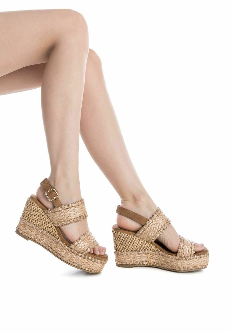 Sandali con zeppa caratterizzati da un design in paglia intrecciata beige, cinturino alla caviglia regolabile e punta aperta. Parte superiore testurizzata e suola robusta.