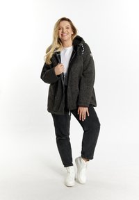 Tamno siva puffer jakna s kapuljačom, prednjim zatvaračem i bočnim džepovima. Nošena preko bijele majice i crnih traperica, upotpunjena bijelim tenisicama.