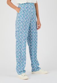 Patronenbroek met een blauw en groen bloemenpatroon op een witte achtergrond, met een hoge taille en zijzakken.