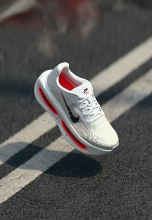 Hvid atletisk sko med en struktureret mesh-overdel, sort swoosh-logo, rød inderside og synlig luftdæmpning i sålen.