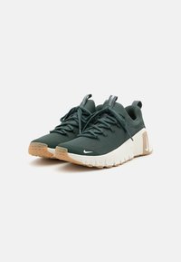 Zelene atletske tenisice s teksturiranim gornjim dijelom, bijelim međuslojem i gumeni potplat. Imaju čipke i petni trak za lakše obuvanje. Nike logo je vidljiv.