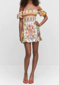 Robe épaules dénudées avec motifs floraux colorés, ourlet à volants et bretelles spaghetti réglables. En tissu léger. Sandales rouges.