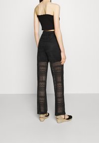 Top noir sans bretelles associé à un pantalon large en dentelle noire avec un motif ondulé. Porté avec des espadrilles noires.