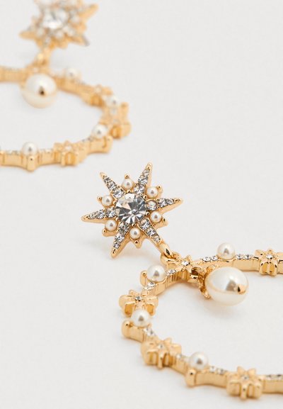 Σκουλαρίκια με χρυσό τόνο που διαθέτουν σχέδια αστεροειδούς, διάφανα κρύσταλλα και διακοσμητικές πέρλες. Κυκλικό σχήμα με περίτεχνα λεπτομέρειες και πινελιές.