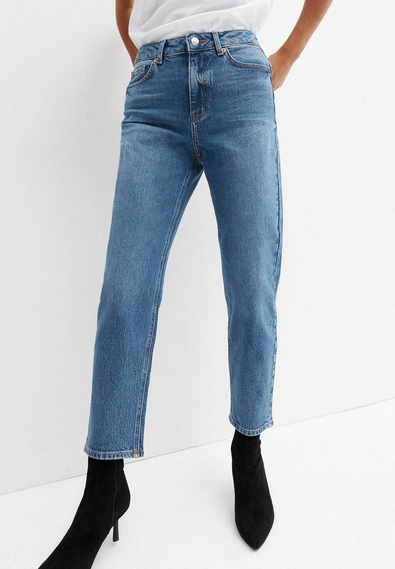 Ljusblå denimjeans med hög midja, rak skärning och fransad fåll, kombinerat med svarta ankelstövlar.