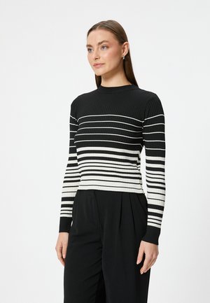 Gestreifter, schwarz-weißer, gerippter Pullover mit langen Ärmeln, rundem Hals und tailliertem Design, kombiniert mit dunklen Hosen.