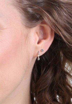 Boucles d'oreilles en argent, comprenant des créoles et des clous, présentées sur l'oreille, avec une finition polie et des détails complexes sur la créole.