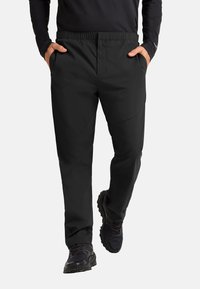 Pantalons noirs, légers, avec une taille élastique et des poches latérales, design à jambes droites et finition lisse, associés à des chaussures de sport noires.