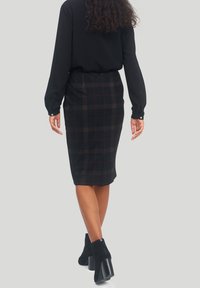 Svart rutig blyertskjol med en figurnära design, medellång. Har ett texturerat tyg och en diskret siddragkedja. Stylar med ankelboots.