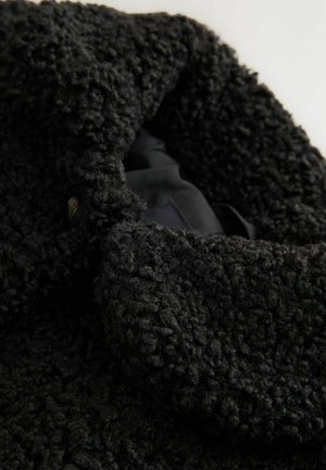 Schwarze Texturjacke mit einem plüschigen, lockigen Äußeren und einem glatten Innenfutter. Der Kragen ist weit und hat eine Knopfdetaillierung.