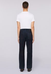 Donkerblauwe broek met opgestikte zakken, rechte pijpen en een gestructureerde stof. Gdragend met een effen wit T-shirt. Achteraanzicht getoond.