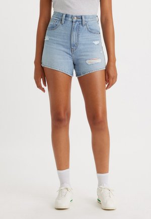 Shorts de denim azul claro con dobladillo deshilachado y acentos desgastados, diseño de tiro alto, combinados con zapatillas blancas y calcetines hasta la altura del tobillo.