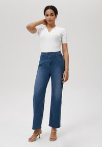 Hooggeplaatste denim broeken in medium blauw, met knopen aan de voorkant, een rechte pijpontwerp en een gladde textuur. Gecombineerd met een witte geribbelde top.