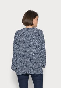 Blusa floral azul-marinho com decote redondo e mangas longas. Apresenta um tecido leve e pequenos padrões florais brancos por toda a parte.
