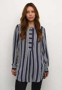 Blusa de rayas azul marino y blanca de manga larga con cuello redondeado, botones frontales y un ajuste ligeramente holgado, hecha de tejido ligero.