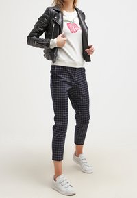 Černá kožená motorkářská bunda, šedá mikina s červenou grafikou jablka, tmavě modré kostkované kalhoty a bílé tenisky na suchý zip.