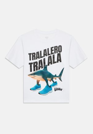 Camiseta blanca con el texto "TRALALERO TRALALA" y un gráfico de un tiburón con zapatillas azules caminando, logo de "Italian Brainrot" abajo.
