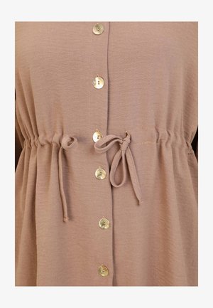 Lysebrun, struktureret stofoverdel med en indsnævret talje, der har gyldne knapper foran og snore i taljen til justerbar pasform.