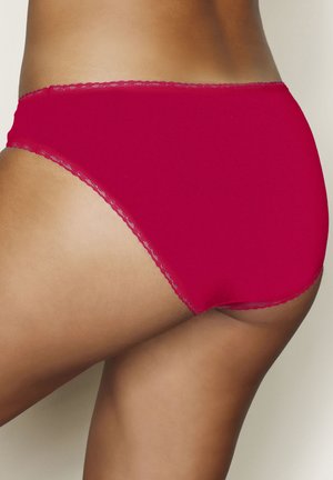 Frau trägt rote Baumwoll-Unterwäsche mit hohem Bund und Spitzenbesatz, gezeigt von hinten und seitlich vor einfarbigem Hintergrund.