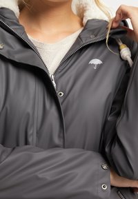 Gray waterproof jacket with a fleece-lined hood, silver umbrella logo on the chest, and snap buttons for closure. Smooth, sleek texture.