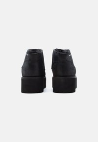 Botas de tobillo de ante negro con una suela de plataforma gruesa, que cuentan con una lengüeta y una textura suave. Vista trasera mostrada.